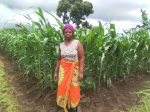 Chrissy, a member of a Village Savings and Loans group, stands in front of a maize field.