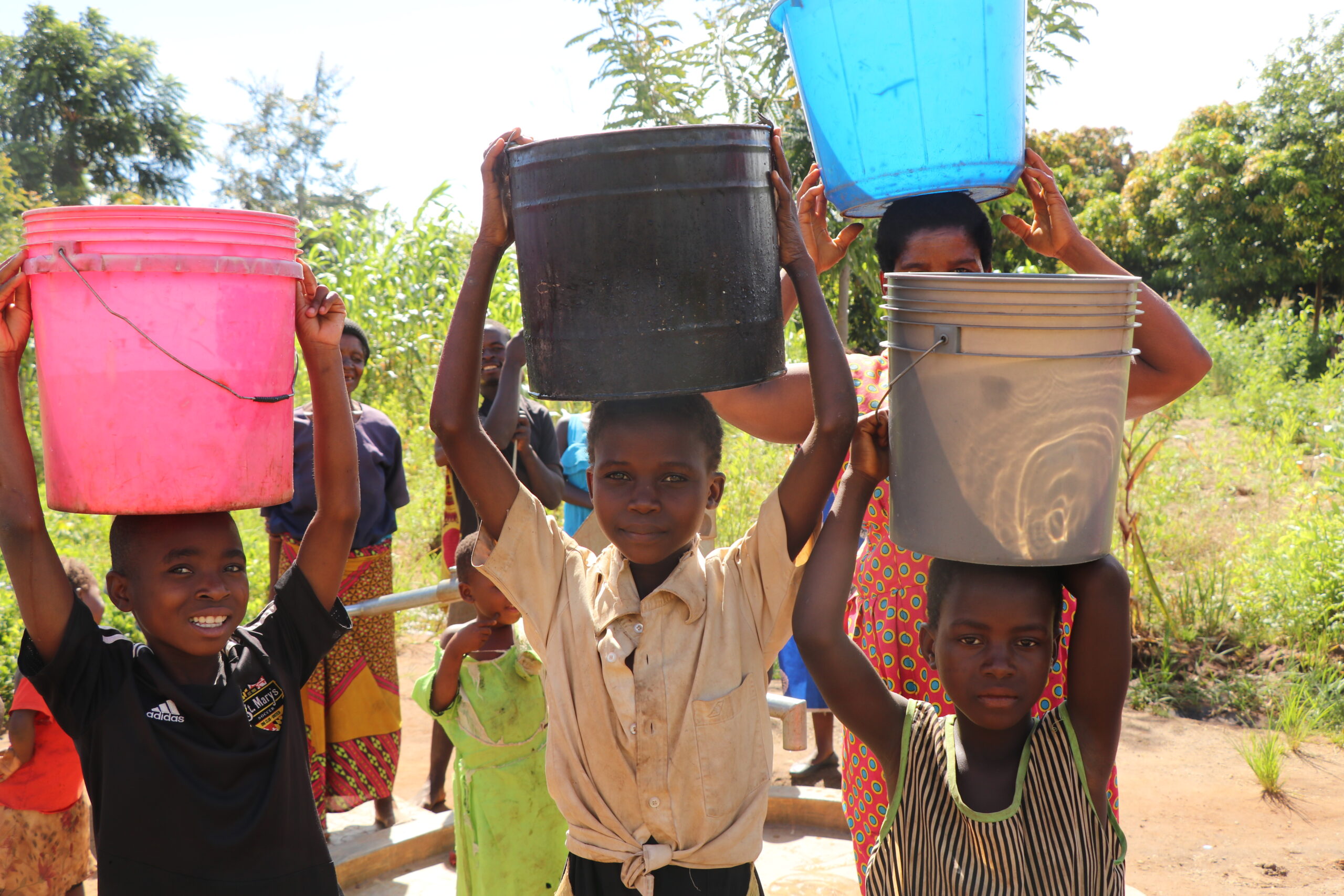 Kids in Malawi hold buckets of water on their heads