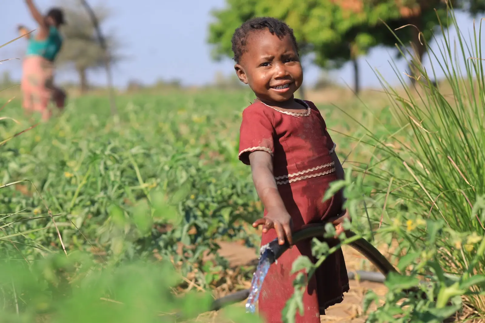 A young girl waters plants from a hose in Malawi